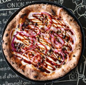 The Mancini pizza has fresh mozzarella, pistachios, red onions, fresh rosemary, and extra virgin olive oil and optional balsamic reduction.